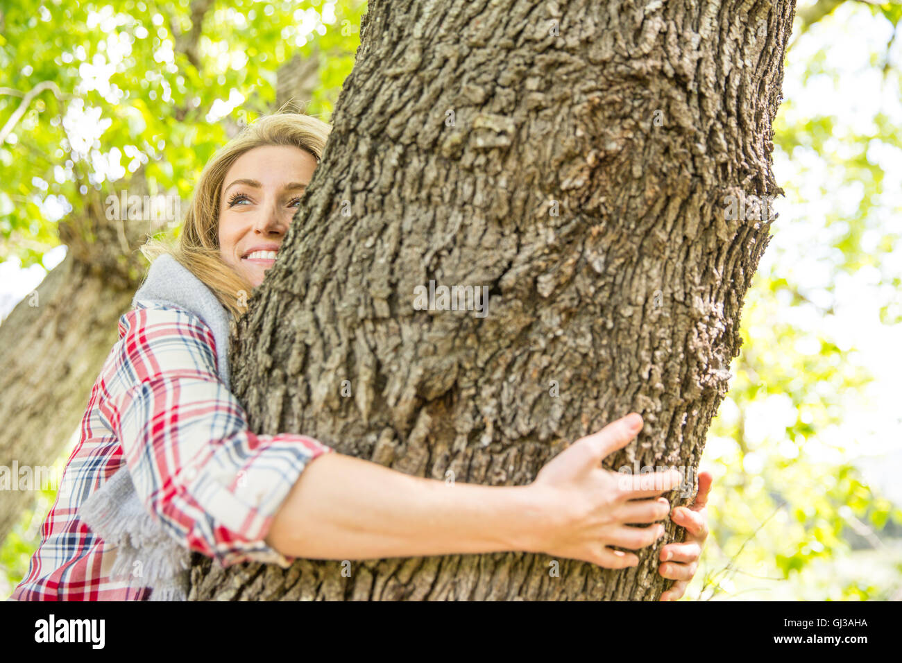 Frau Baum lächelnd umarmen Stockfoto