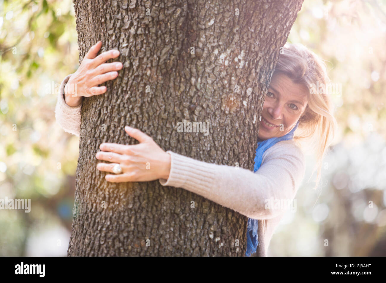 Frau umarmt Baum Blick auf die Kamera zu Lächeln Stockfoto