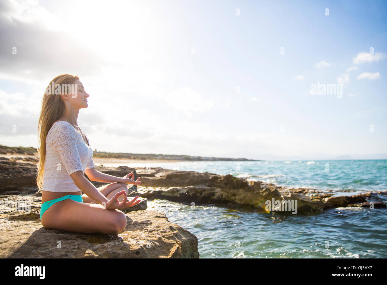 Junge Frau sitzt auf den Felsen, auf dem Seeweg in Yogaposition Stockfoto