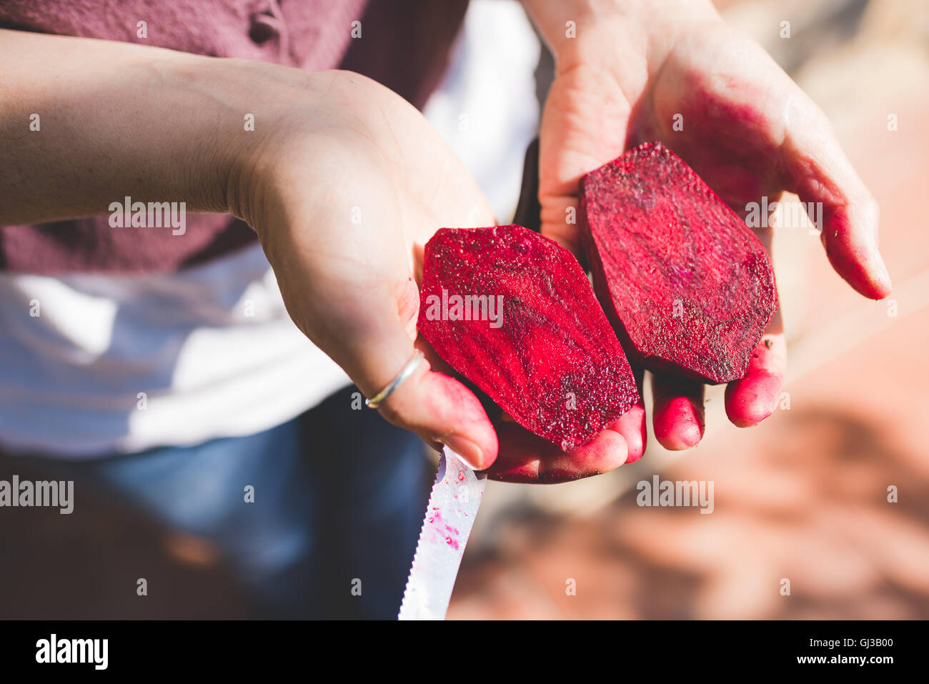 Zarte Frauenhand halbierte frische rote Beete im Garten halten Stockfoto