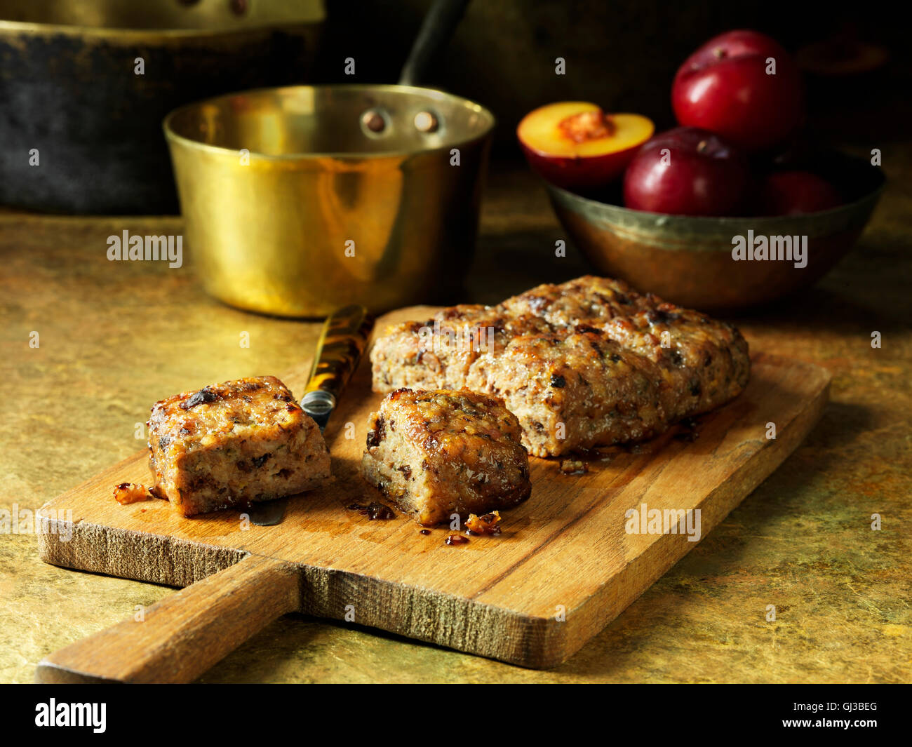 Schweinefleisch und Zucker Plumpudding auf Schneidbrett aus Holz, goldne Topf, Schüssel mit Pflaumen Stockfoto