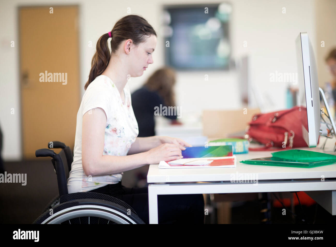 Junge weibliche Studentin mit Rollstuhl Lesung Notizen am Schreibtisch Stockfoto