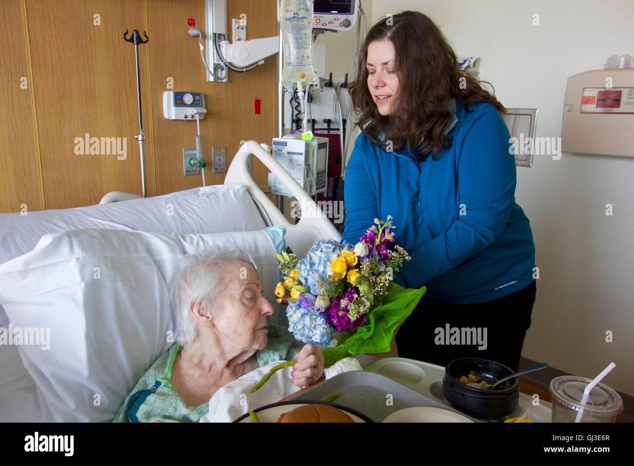 Eine Frau, die ihrer kranken Großmutter im Krankenhaus besuchen hält einen Blumenstrauß für die ältere Frau zu riechen. Stockfoto