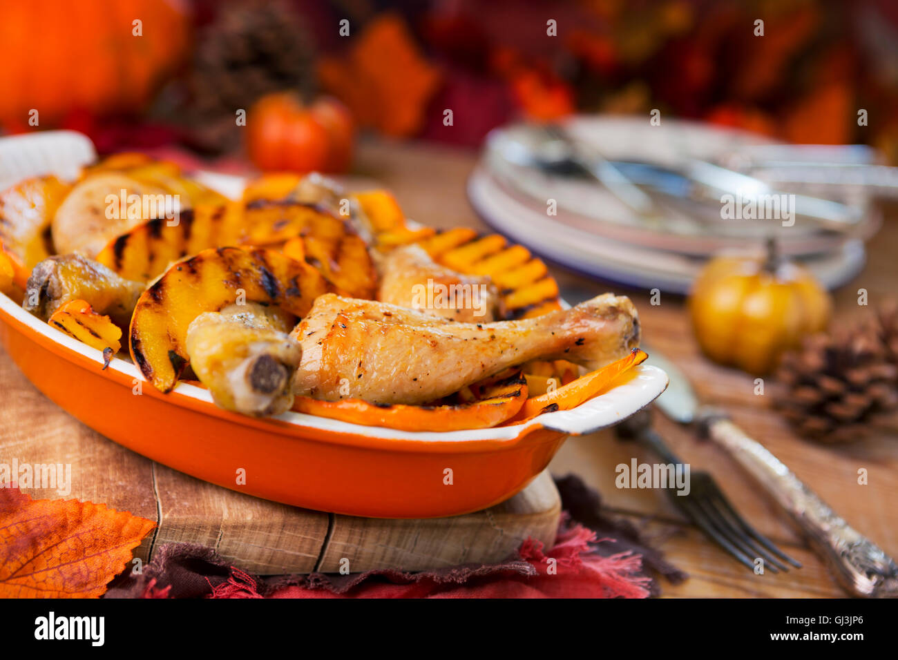 Eine Kasserolle mit Backofen gebratenes Huhn und gegrilltem Kürbis auf einem rustikalen Tisch mit herbstlichen Dekorationen. Stockfoto