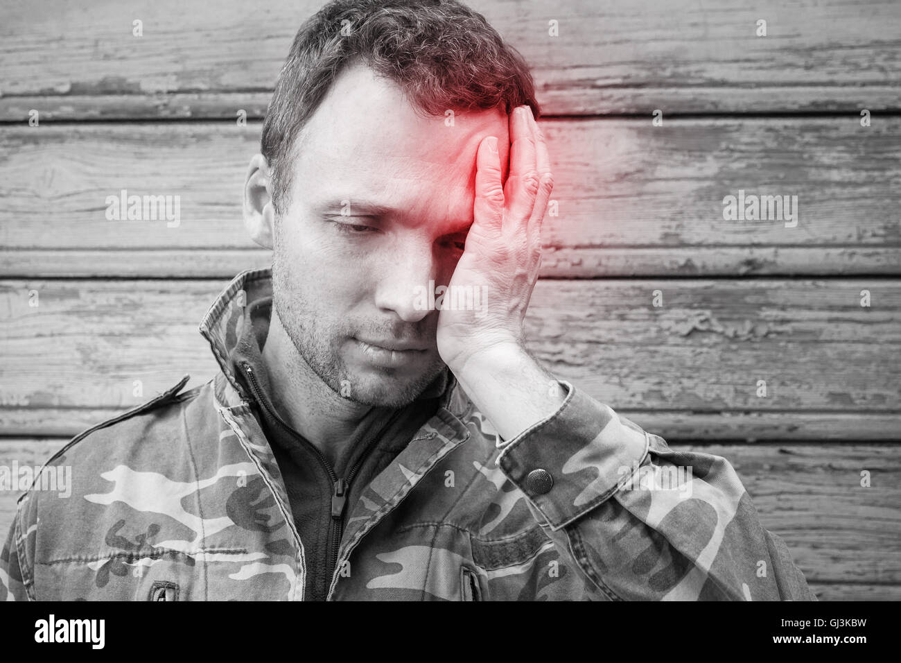 Kaukasische junge Mann mit Kopfschmerzen in Tarnung. Stilisierte Foto schwarz / weiß mit roten lokalen Schmerzen vor Ort Stockfoto