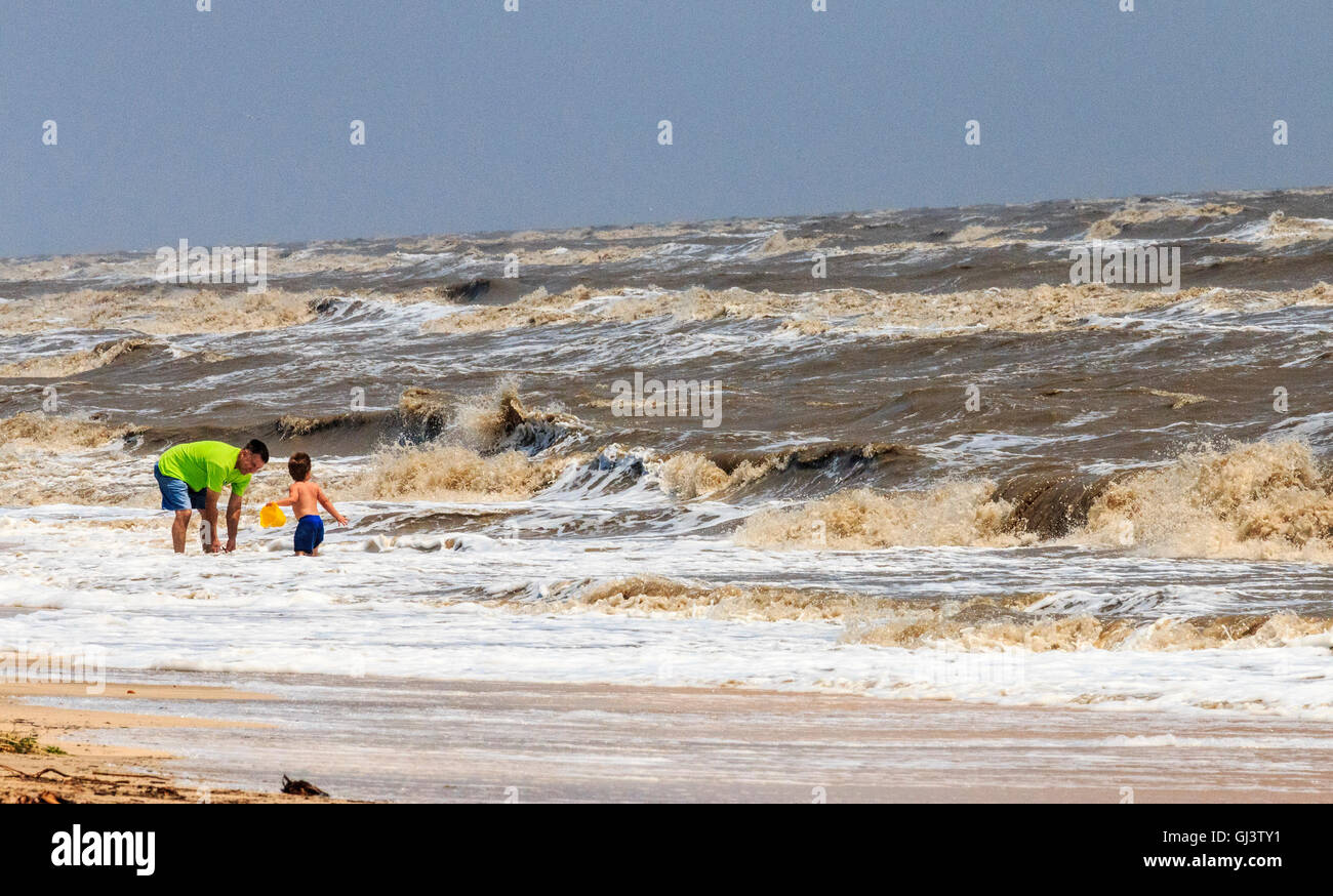 Kleiner Junge spielt in raue Brandung mit Vater während einem windigen Tag am Rutherford Strand an der Küste des Golfs von Mexiko in Louisiana. Stockfoto