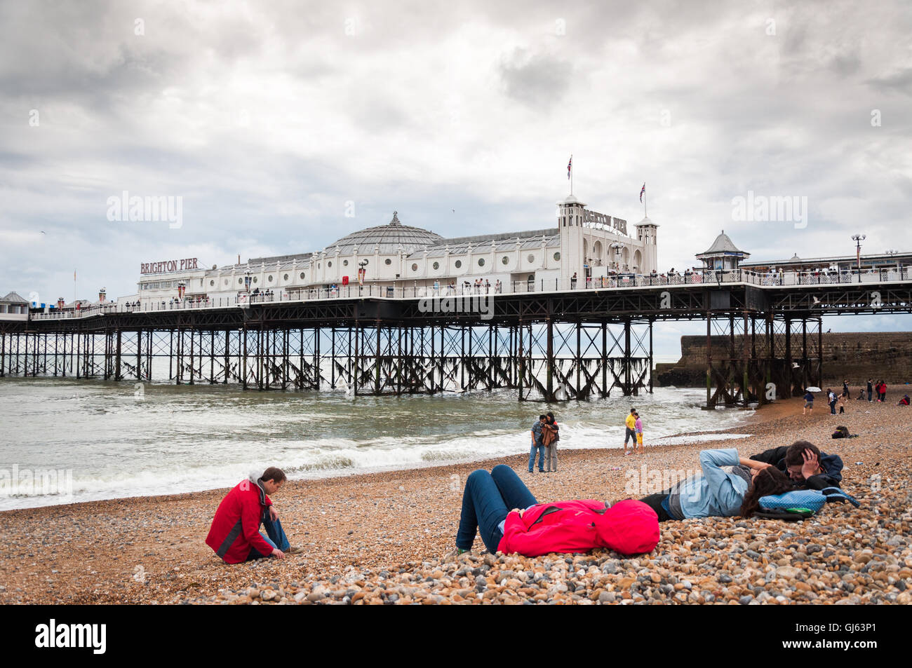 An einem kalten Sommertag in Brighton, East Essex, Großbritannien, sonnenbaden Menschen am Kemptown Brighton Beach in der Nähe des Brighton Piers ab 2012 in Jacken Stockfoto
