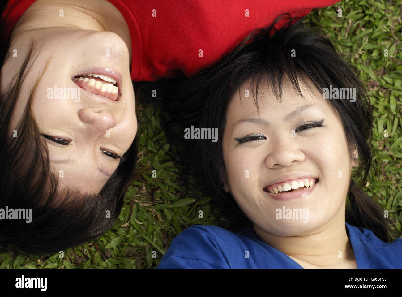 Zwei glückliche asiatische Teen Mädchen auf Rasen Porträt tragen rot und blau liegend Stockfoto