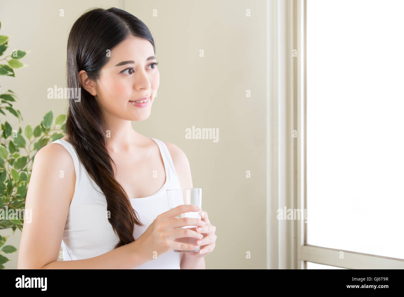Schöne asiatische Frau Blick aus Fenster und Trinkwasser indoor Stockfoto