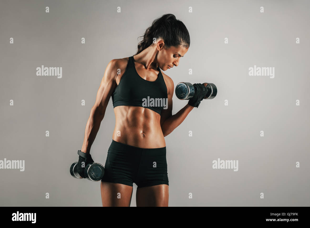 Einzelne gesunde sportliche Frau mit muskulösen Körper heben Chrom finish Hantel Gewichte über grauen Hintergrund mit Textfreiraum Stockfoto