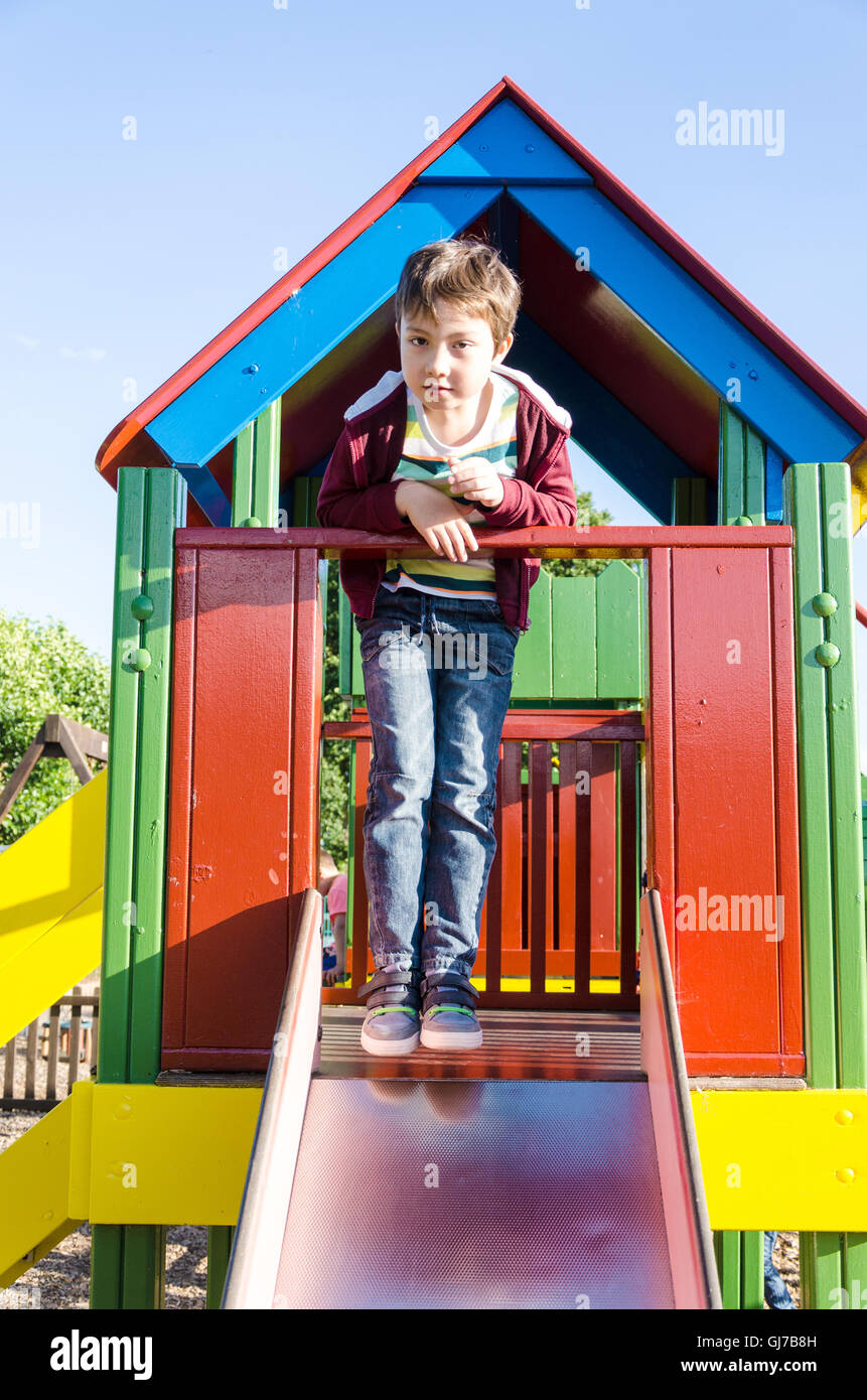 Ein kleiner Junge posiert für ein Foto am oberen Rand einer Folie in einen Kinderspielplatz. Stockfoto