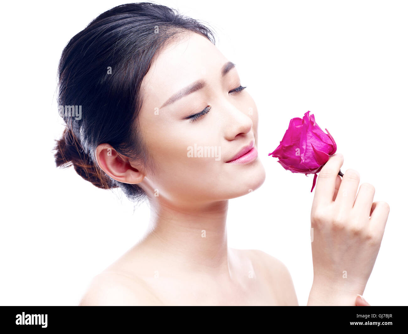 junge und schöne asiatische Frau genießen Sie den Duft von einer roten Rose, isoliert auf weißem Hintergrund. Stockfoto