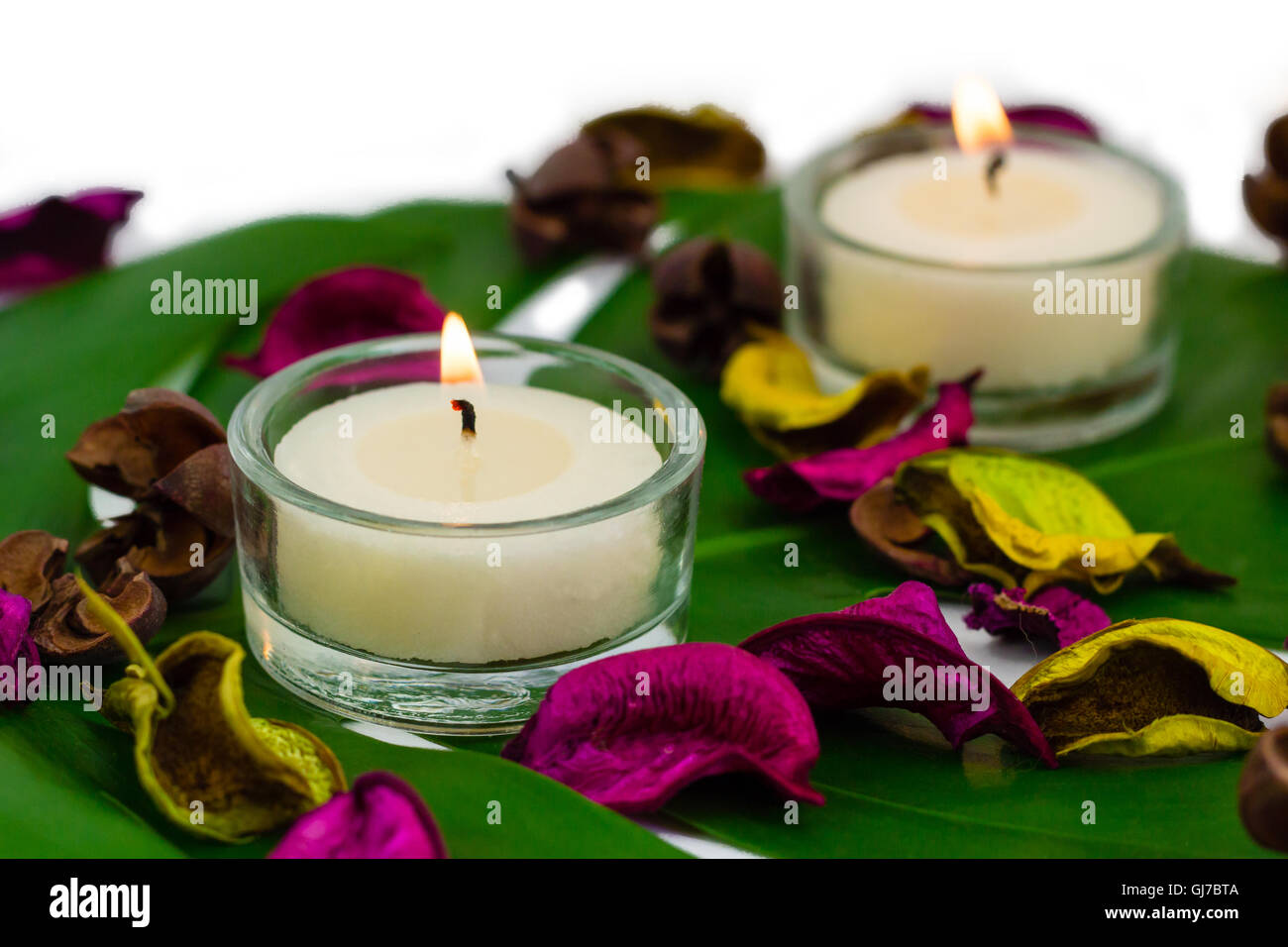Frische bunte Zusammensetzung der zwei brennenden Kerzen, duftenden Potpourri an Monstera Blatt Stockfoto