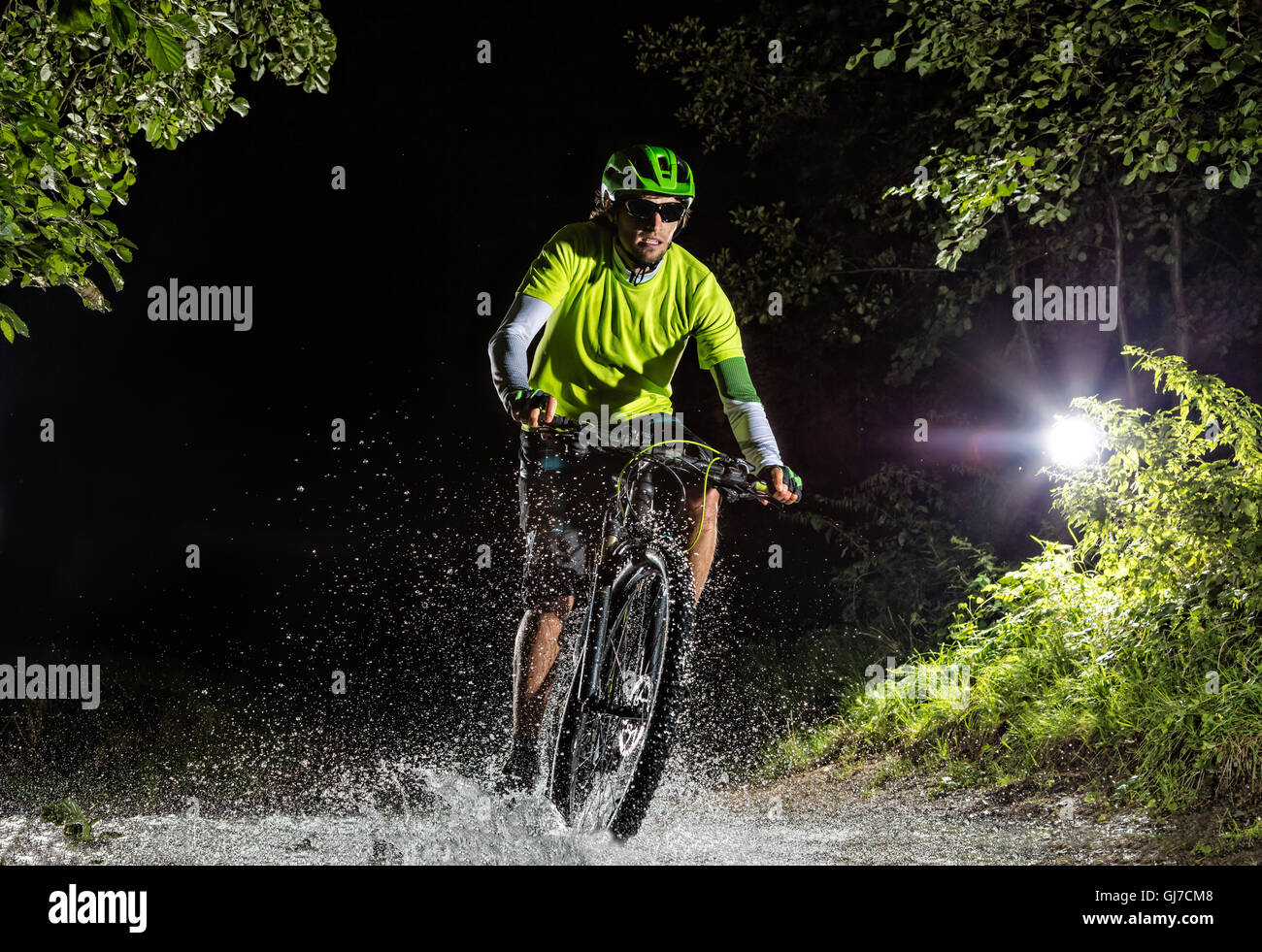 Mountainbiker bei Nacht Fahrt durch Wald Stream und spritzt Wasser herum. Frontansicht Stockfoto