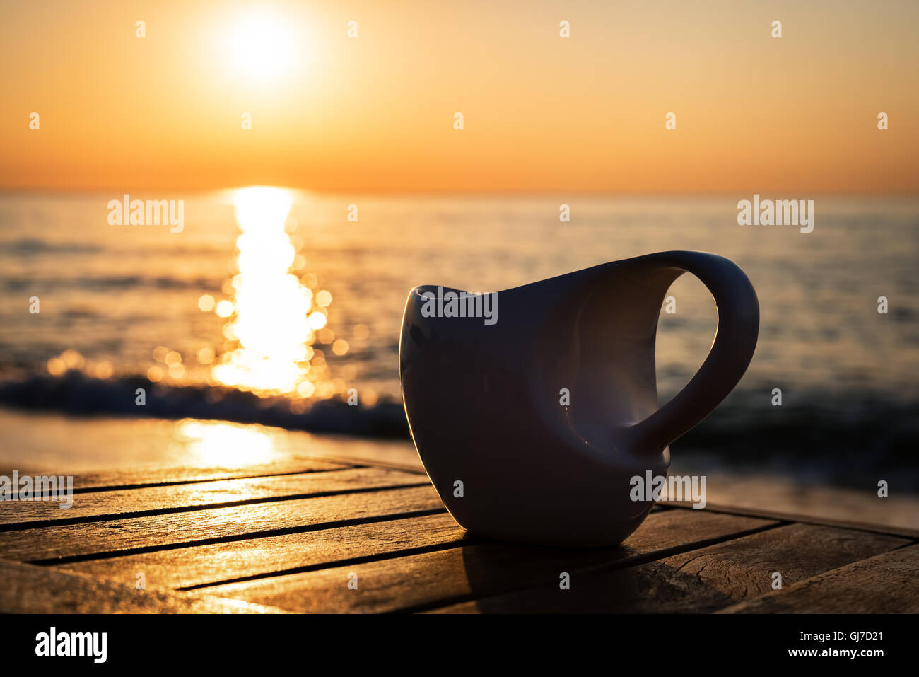 Kaffeetasse auf Holztisch bei Sonnenauf- oder Sonnenuntergang Strand Stockfoto