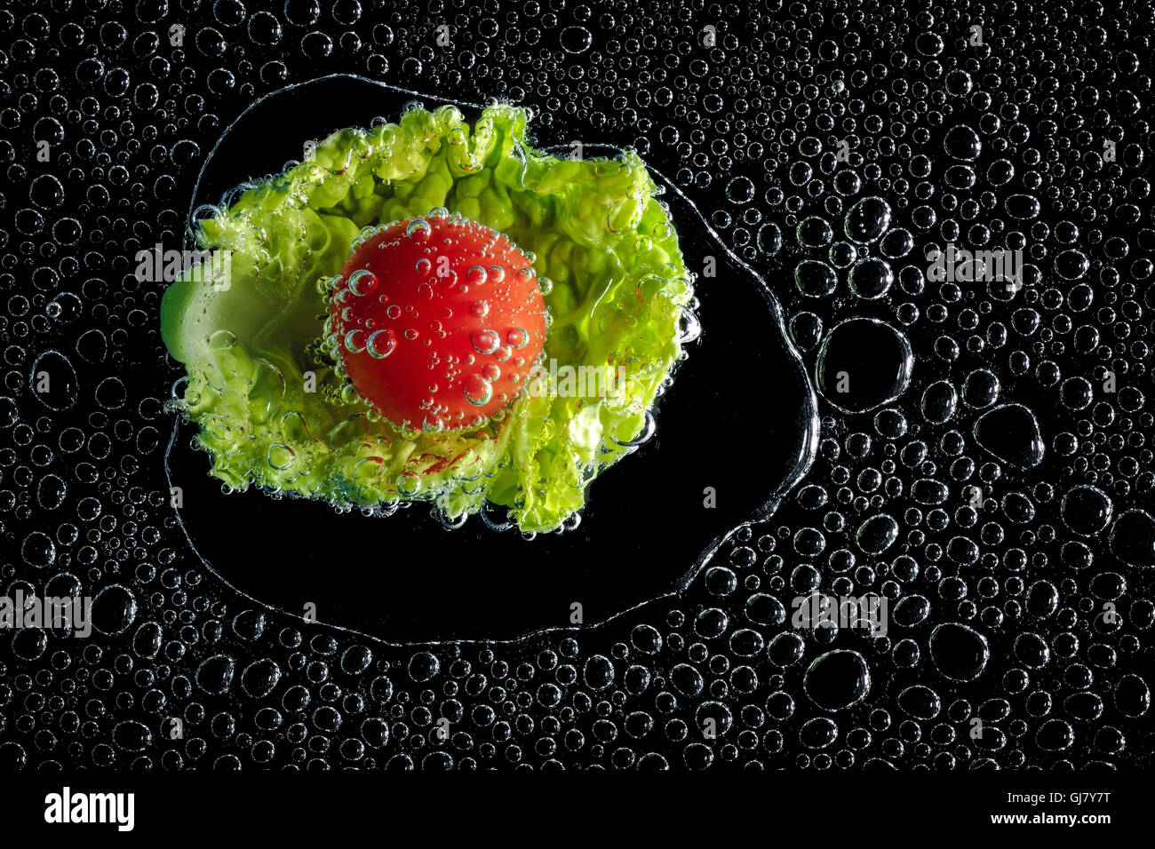 Salat und Tomate in Mineralwasser, eine Reihe von Fotos. Close-up kohlensäurehaltiges Wasser vor schwarzem Hintergrund Stockfoto