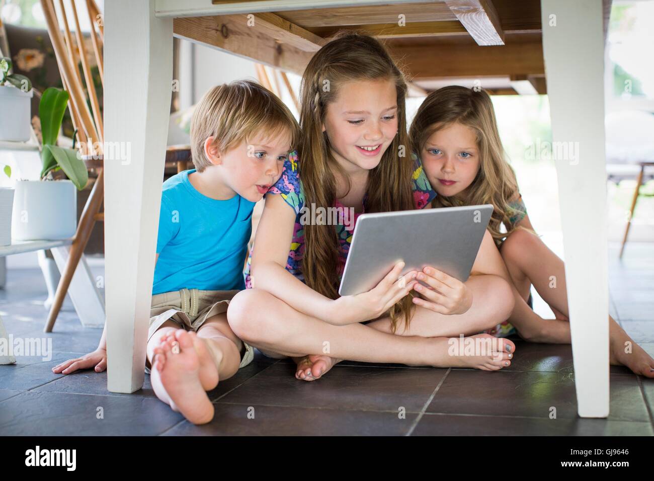 EIGENTUM FREIGEGEBEN. -MODELL VERÖFFENTLICHT. Drei Geschwister unter Tisch mit digital-Tablette. Stockfoto