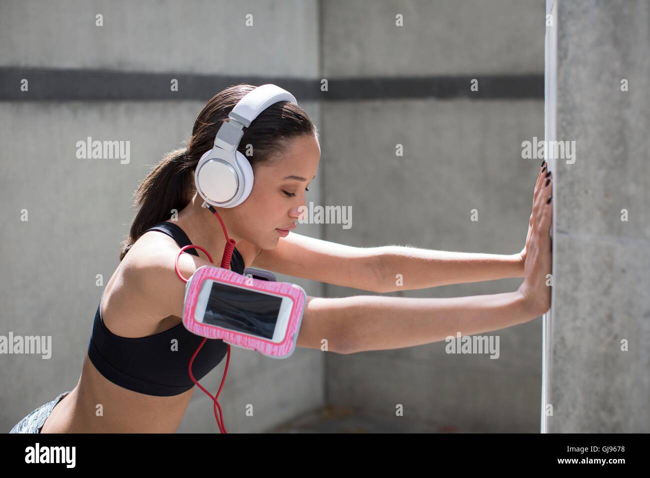 -MODELL VERÖFFENTLICHT. Junge Frau trägt Kopfhörer und Sport Band Dehnung gegen die Wand. Stockfoto