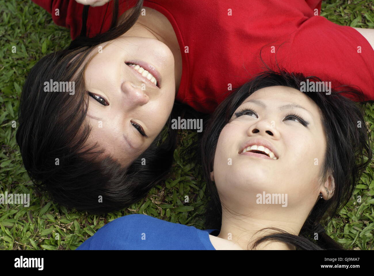 Zwei glückliche asiatische Teen Mädchen auf Rasen Porträt tragen rot und blau liegend Stockfoto