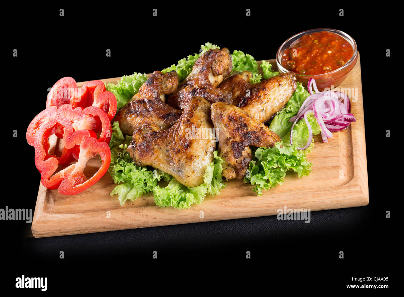 Hähnchenflügel mit Sauce und Gemüse auf Holztisch. Stockfoto