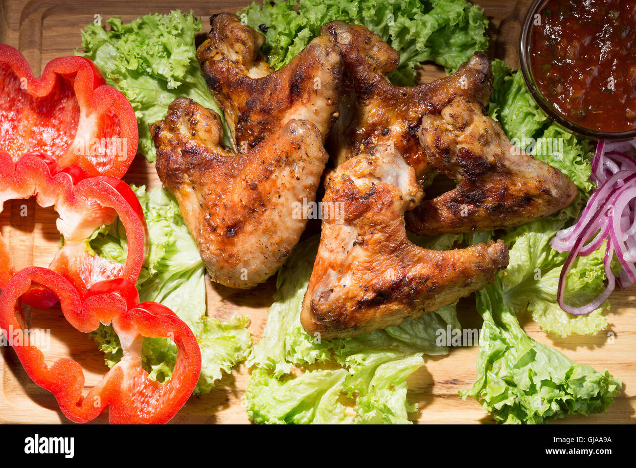 Hähnchenflügel mit Sauce und Gemüse auf Holztisch. Stockfoto