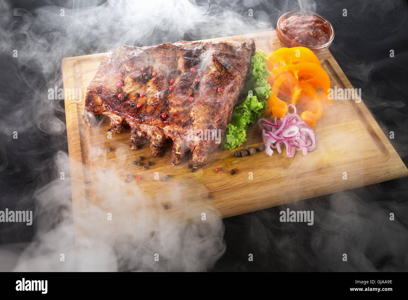 Grill-Rippchen mit Rauch mit Sauce und Gemüse auf Holztisch. Stockfoto