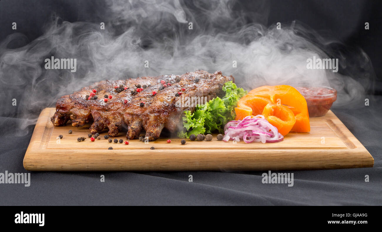 Grill-Rippchen mit Rauch mit Sauce und Gemüse auf Holztisch. Stockfoto