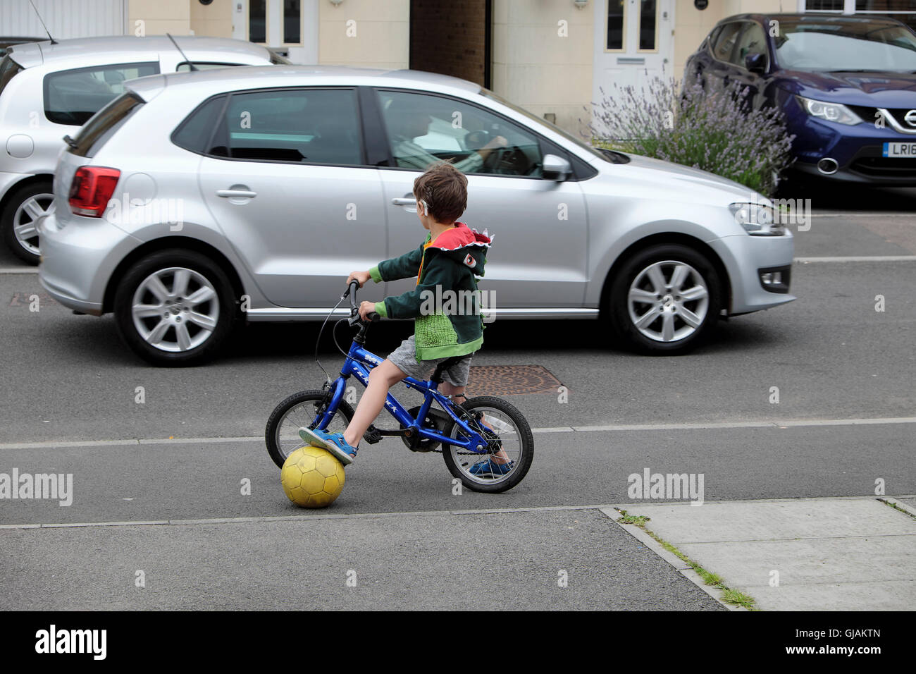 Kleine Kinder spielen mit Fußball auf dem Fahrrad in der Nähe von PKW-Verkehr  in der Straße in DE KATHY DEWITT Stockfotografie - Alamy