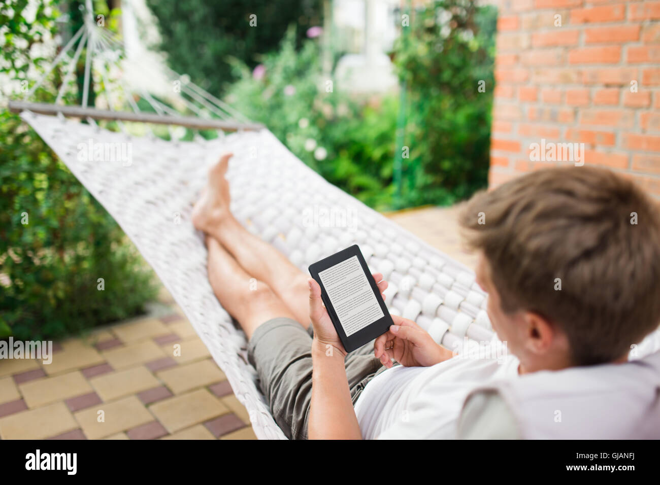 Mann mit e-Book mit Lorem Ipsum Text auf dem Bildschirm beim Entspannen in der Hängematte. Stockfoto
