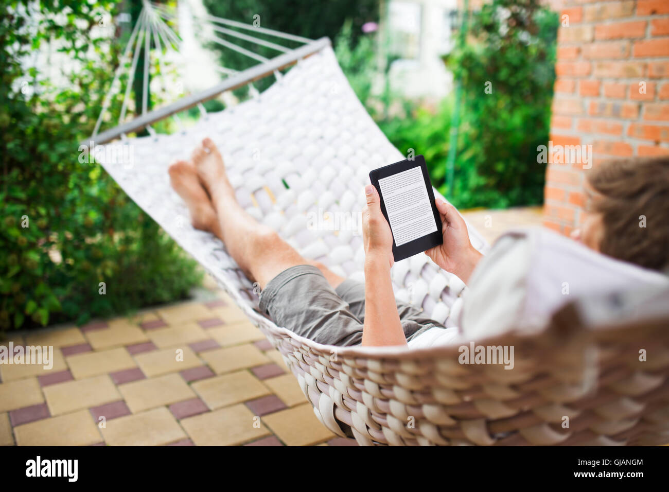 Mann mit e-Book mit Lorem Ipsum Text auf dem Bildschirm beim Entspannen in der Hängematte. Stockfoto