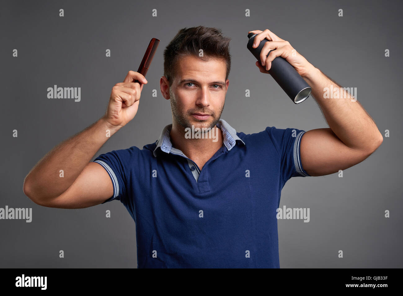 Ein hübscher junger Mann lächelnd, während Sie einen Kamm und ein Haarspray in seiner Hand hält. Stockfoto