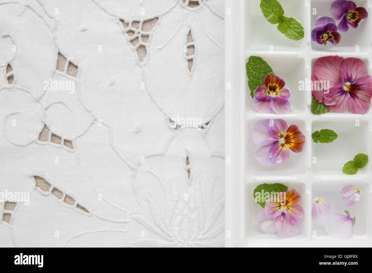 Essbare Blumen und Minze in Würfel Eiswürfelschale auf weiße Vintage Leinen-Hintergrund Stockfoto