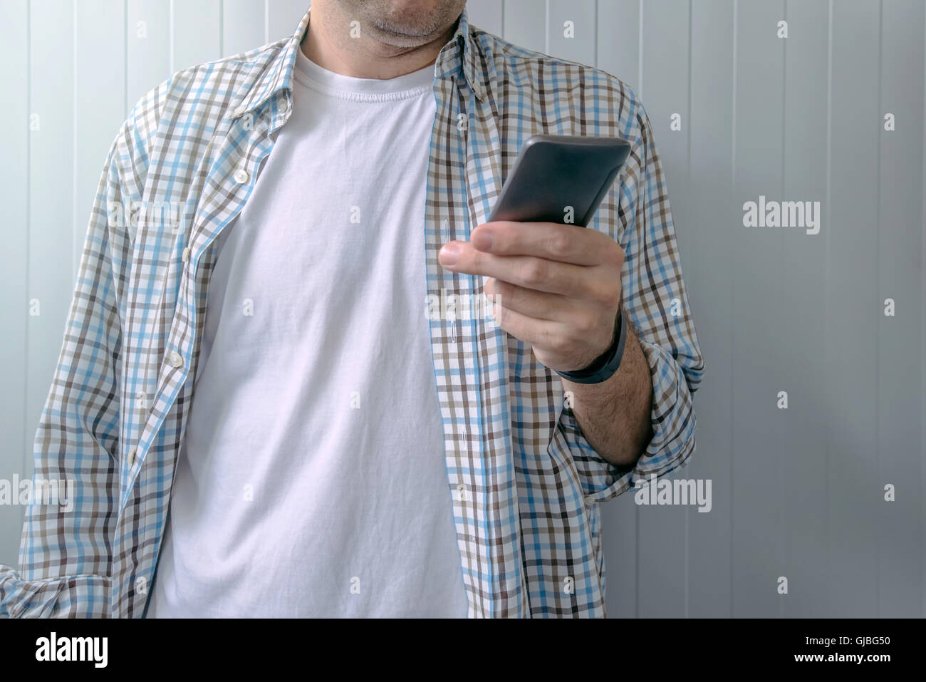 Gelangweilt legerer Mann im karierten Hemd mit Handy, Zeit zu verschwenden Stockfoto