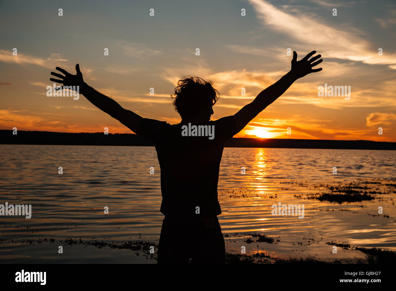 Glücklicher Mann Silhouette mit den Händen bis auf den Sonnenuntergang Hintergrund am Strand Stockfoto