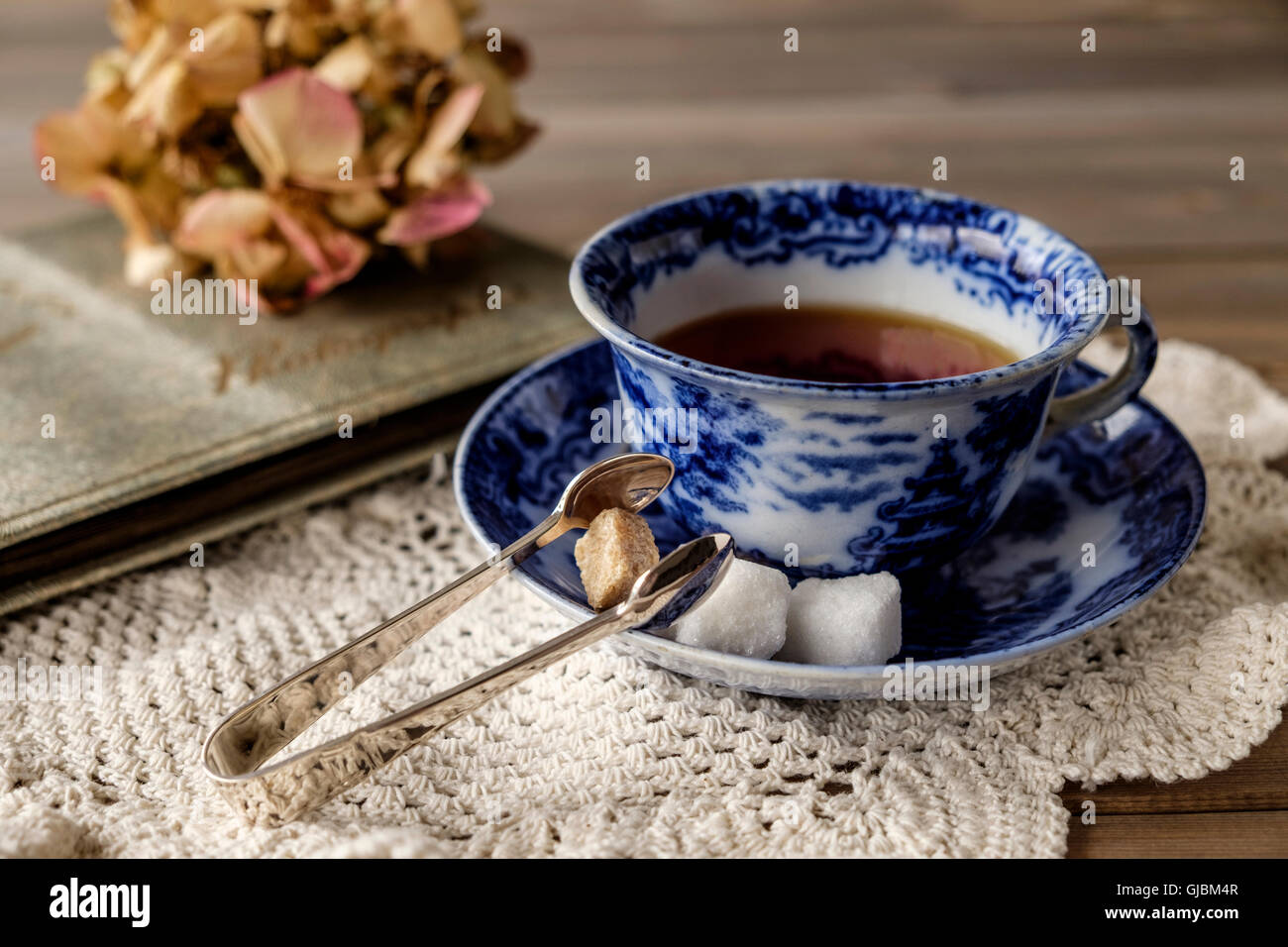 Nahaufnahme der Antike China-blauen und weißen Tasse und Untertasse mit Tee auf Lace-Tuch auf Holztisch mit aus Fokus verblasst Blume Stockfoto