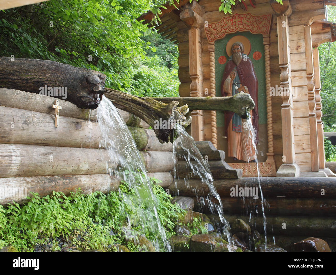 Wasser aus der Quelle durch die Kanäle der Baumstämme auf dem Hintergrund der Kapelle. Stockfoto