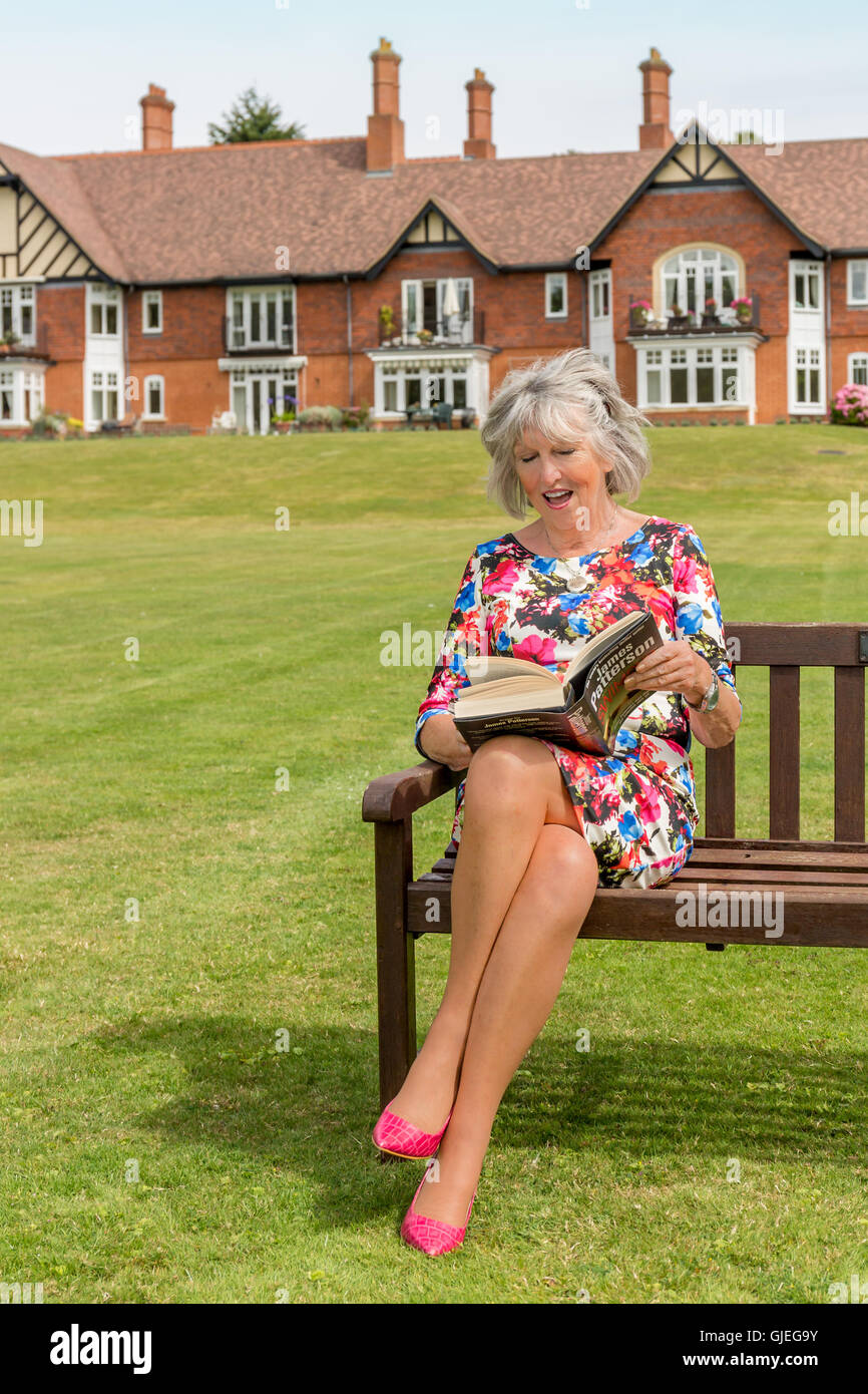 Glamouröse pensionierte Frau sitzen auf einer Bank am Fluss, ein Buch zu lesen Stockfoto