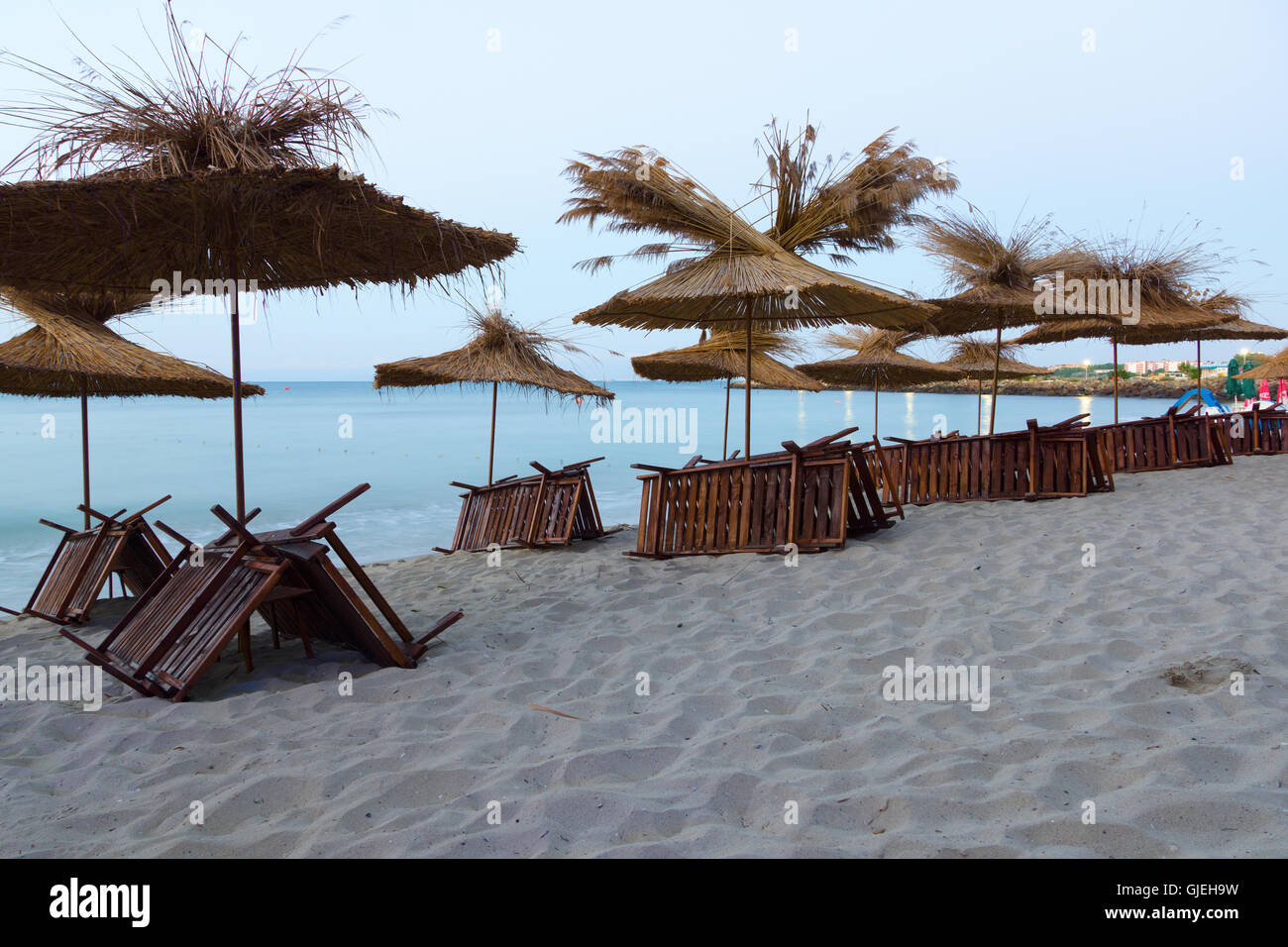 strohgedeckte Sonnenschirme und Liegestühle gestapelt in der Nacht am Strand warten auf morgen Besucher Stockfoto