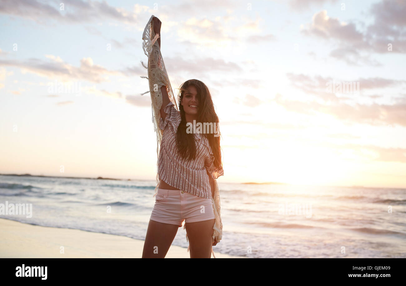 Schöne weibliche Model Spaß am Strand. Attraktive junge Frau am Strand bei Sonnenuntergang mit ihren erhobenen Händen stehen. Stockfoto