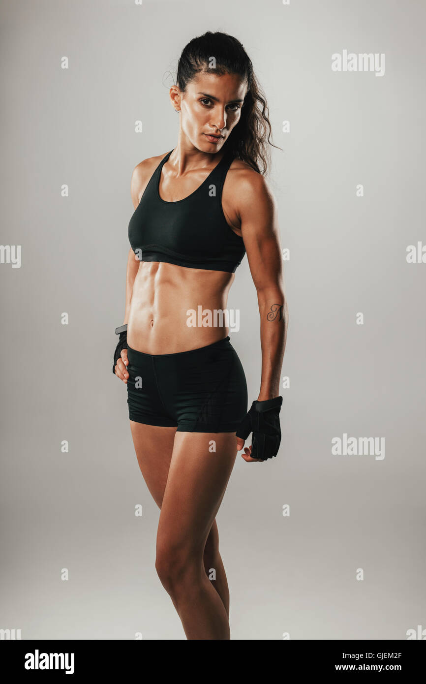 Hübsche Frau im sportlichen shorts Blicke in die Kamera beim Posieren vor einem grauen Hintergrund Stockfoto
