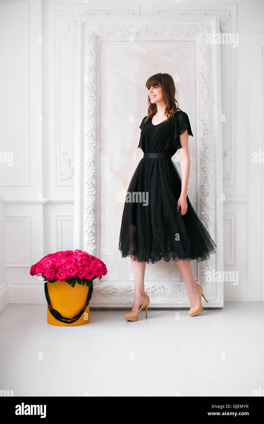 Schöne junge Mädchen. in einem schwarzen Kleid und Schuhe mit hohen  Absätzen. duftende Blüten mit lila Rosen in Hutschachtel zur verputzten  Wand Stockfotografie - Alamy