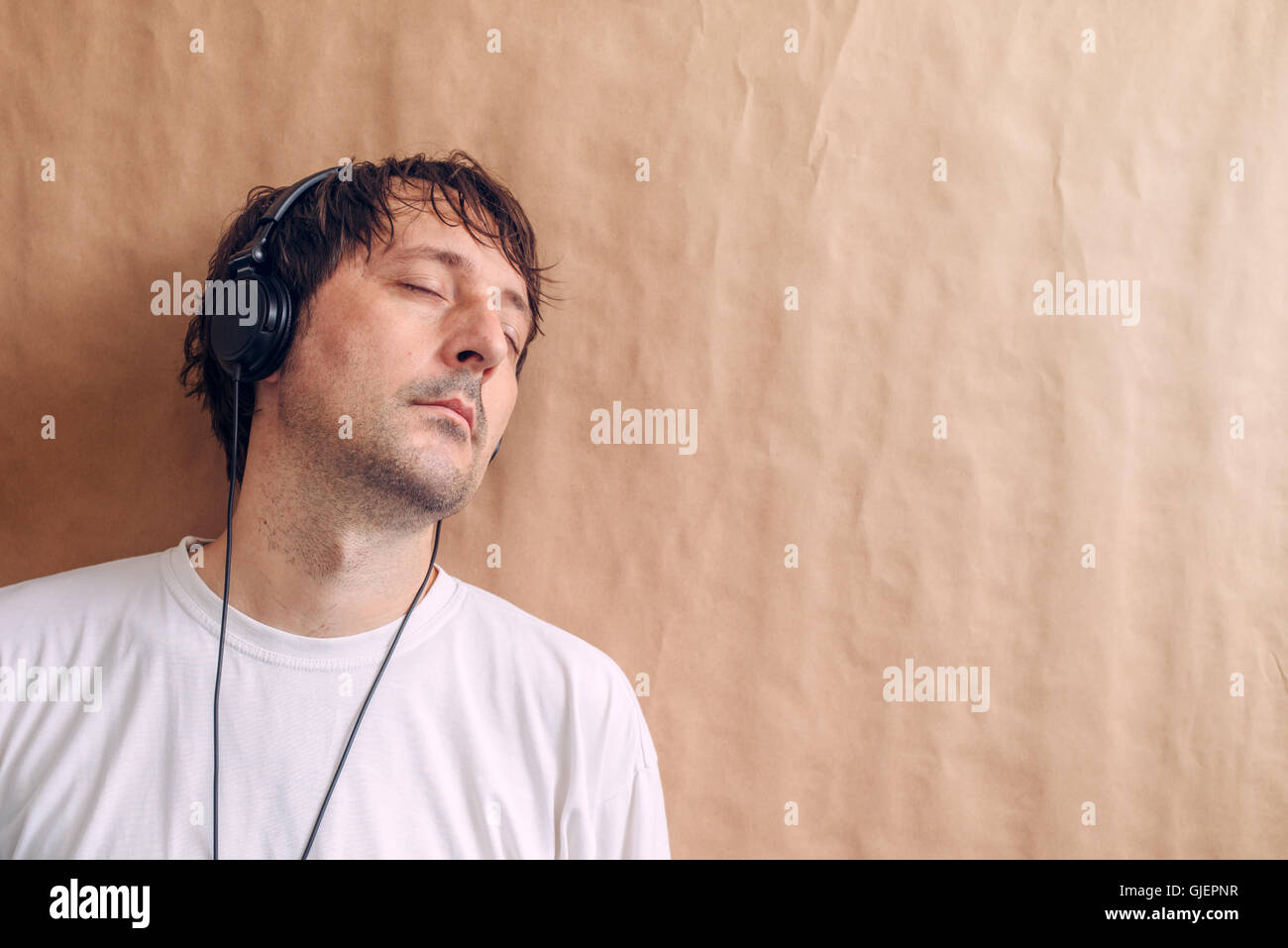 Erwachsene männliche anhören Lieblingsmusik Podcasts über Kopfhörer, Mann mit geschlossenen Augen auf Wand gelehnt und Entspannung zu genießen. Stockfoto