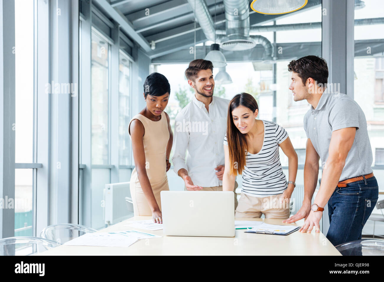 Multiethnische Gruppe der glückliche junge Geschäftsleute stehen und Präsentation mit Laptop im Büro Stockfoto