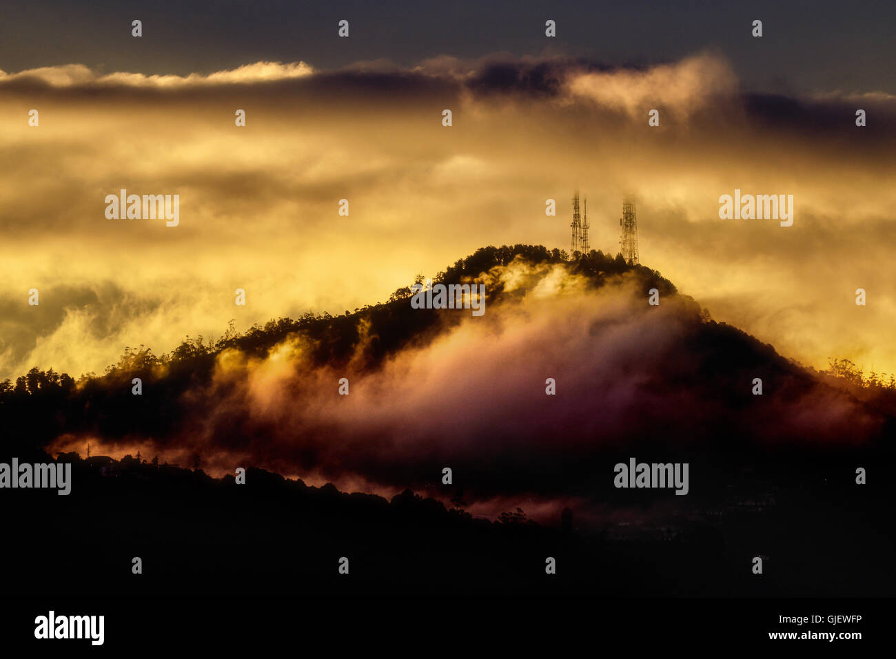 TV-Masten auf einem nebligen Hügel in der Abenddämmerung gegen eine dramatische Bank von Wolken Stockfoto