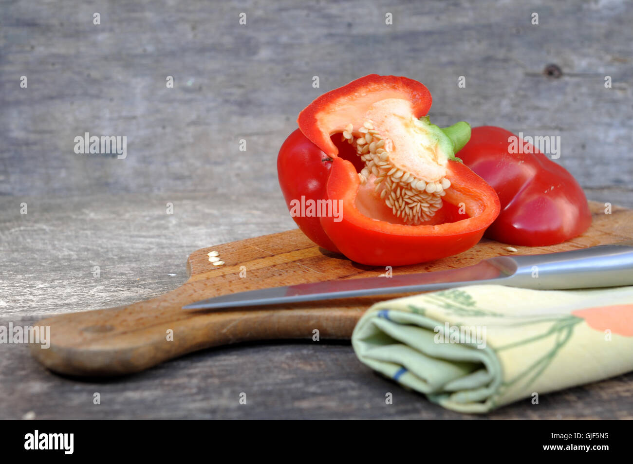 rote Paprika halbieren an Bord mit Messer und Handtuch Stockfoto