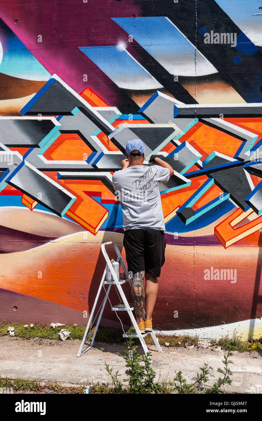 Graffiti-Künstler bei der Arbeit, die Malerei eine alte Mauer, Friedrichshain, Berlin, Deutschland. Stockfoto