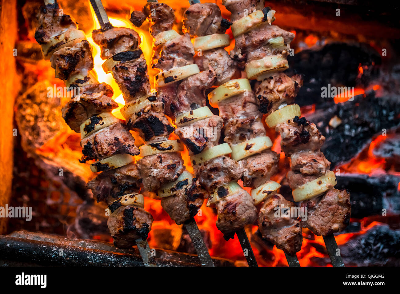 Grill Schweinefleisch-Spieße auf dem heißen Grill Nahaufnahme. Flammen des Feuers und Kohlen im Hintergrund Stockfoto