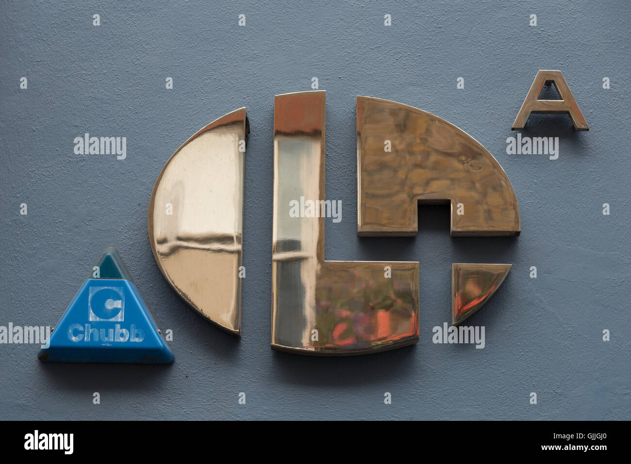 Minimalistische glänzende Messing Nummer 14 A Türnummer und eine blaue Chubb-Alarmanlage, die die Form des A perfekt widerspiegelt. Stockfoto