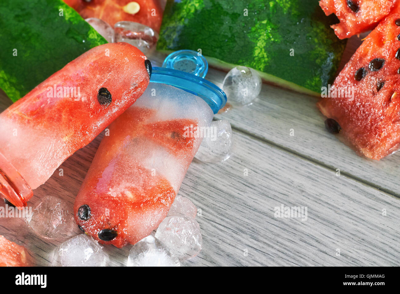Gefrorene Wassermelone Eis am Stiel mit Eiswürfeln und Wassermelone Scheiben auf grauem Hintergrund aus Holz. Konzept-Bild für Sommer-Erfrischung Stockfoto