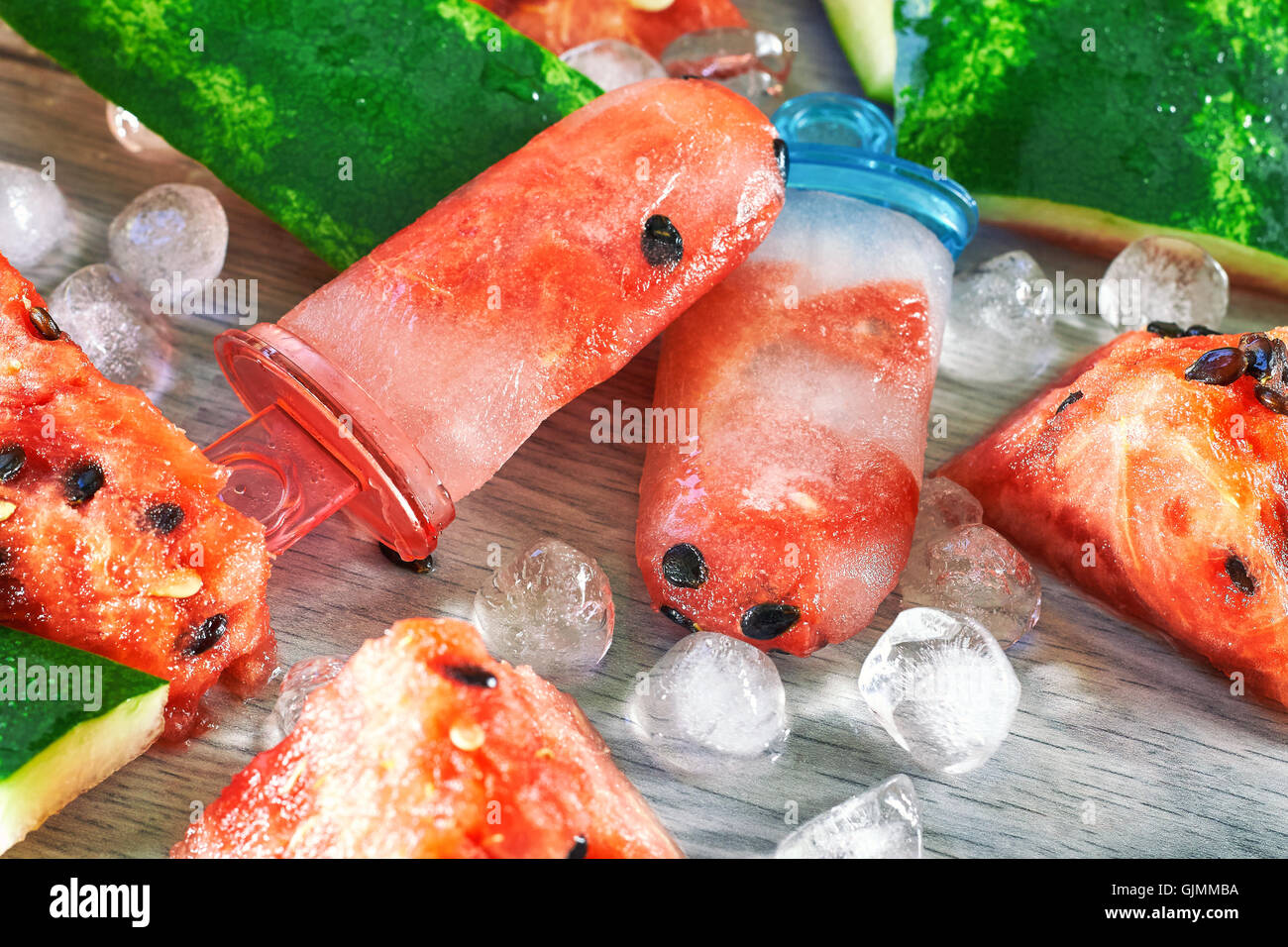 Gefrorene Wassermelone Eis am Stiel mit Eiswürfeln und Wassermelone Scheiben auf grauem Hintergrund aus Holz. Konzept-Bild für Sommer-Erfrischung Stockfoto